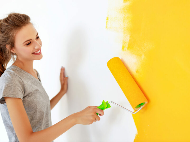 Repair in apartment. Happy young woman paints wall Repair in the apartment. Happy young woman paints the wall with yellow paint